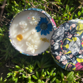 Geurloze kaars van kokos-raapzaadwas in zwart-geel-blauw blikje met bloemen